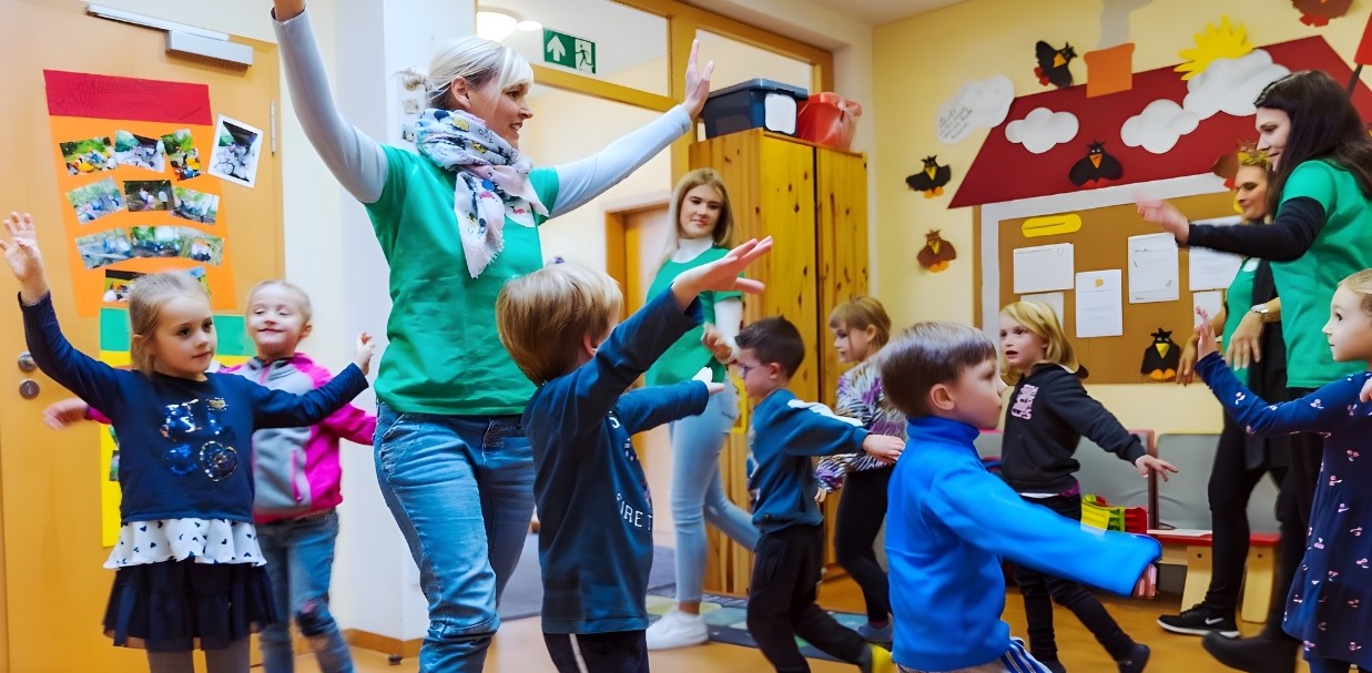 Foto einer Gruppe von Kindern und erwachsenen Personen in einem bunt dekorierten Raum, die gemeinsam tanzen und sich bewegen.