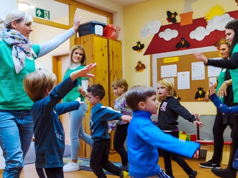 Foto einer Gruppe von Kindern und erwachsenen Personen in einem bunt dekorierten Raum, die gemeinsam tanzen und sich bewegen.